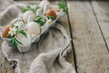 Happy Easter! Easter rustic still life. Natural easter eggs with blooming spring flowers in tray on rural wooden table. Space for text. Simple stylish festive decoration on tableの写真素材