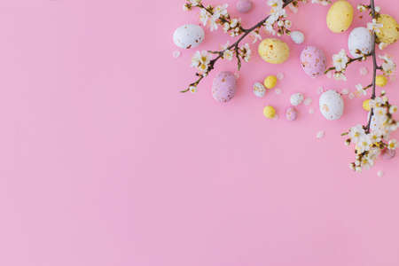Easter flat lay with space for text. Colorful Easter chocolate eggs and cherry blossoms border on...