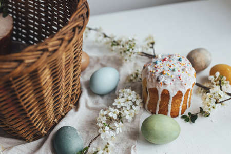 Happy Easter! Stylish easter bread and natural dyed eggs on rustic table with spring blossom and wicker basket. Traditional Easter basket food - easter cake with icing and sprinkles, eggsの写真素材