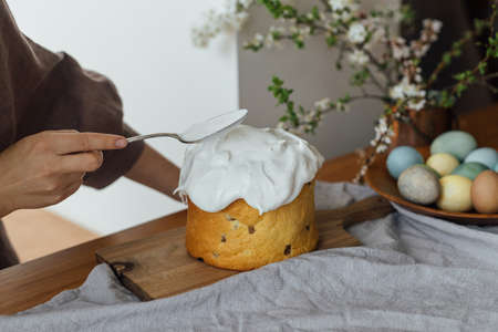Woman decorating homemade easter bread with sugar glaze on rustic table with natural dyed eggs and...