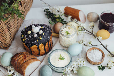 Traditional Easter basket food for festive dinner. Natural dyed easter eggs, stylish easter bread, ham, beets, butter, cheese on rustic wooden table with spring blossoms. Happy Easter!の写真素材