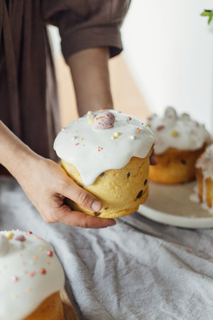 Woman holding baked stylish easter cake with sugar glaze and sprinkles. Homemade easter bread in...