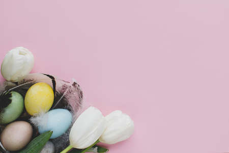 Happy Easter! Stylish easter eggs in nest and flowers flat lay on pink background. Natural dyed...