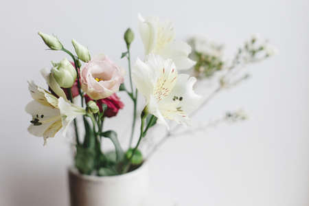 Stylish bouquet in ceramic vase at window, moody image. Beautiful fresh flowers, manuka, alstroemeria, eustoma, eucalyptus floral arrangement. Spring modern bouquet close upの写真素材