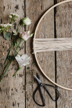 Making stylish spring wreath with beautiful fresh flowers. Wooden hoop, thread, scissors, and flowers on rustic wooden background flat lay. Modern and creative floral handmade decorの写真素材