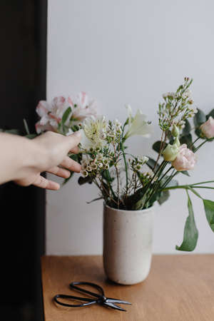 Florist arranging beautiful fresh flowers with scissors on wooden background, floral decor. Hand and stylish bouquet in ceramic vase on wooden windowsill. Spring modern bouquetの写真素材