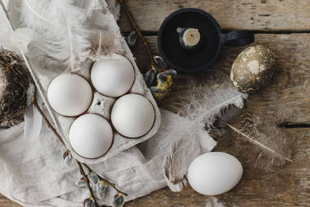 Easter rustic flat lay. Natural eggs in tray, feathers, willow branches, nest on aged wooden table. Stylish Easter rural still life. Simple aesthetics in pastel brown colors. Happy Easterの写真素材