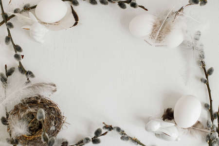 Easter rustic flat lay. Natural eggs, feathers, nest, willow branches frame composition on white wooden table. Space for text. Simple stylish easter background and greeting card. Happy Easterの写真素材