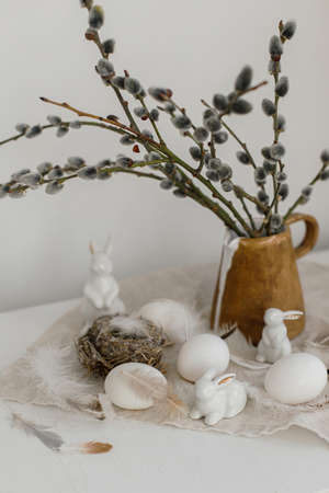Easter rustic still life. Natural eggs, bunny figurines, feathers, nest, willow branches in vase on...