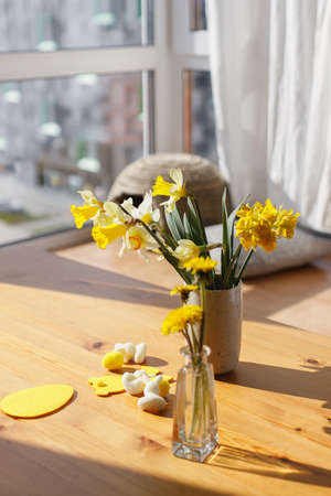 Beautiful daffodils flowers in vase and easter decoration on wooden table in sunny light. Happy Easter! Cute easter eggs, bunny decor, and yellow flowers in sunny roomの写真素材