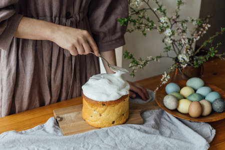Woman decorating homemade easter bread with sugar glaze on rustic table with natural dyed eggs and...