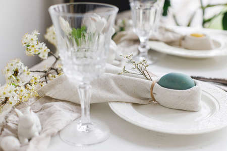 Easter egg in bunny napkin on plate with cutlery, bunny, spring flowers on rustic white table....