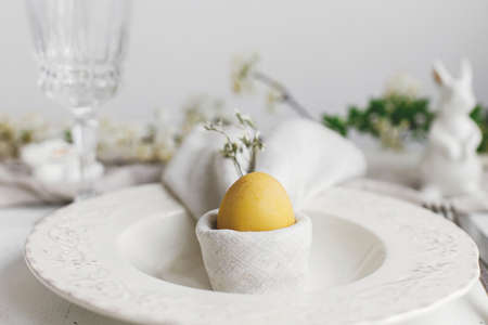 Happy Easter! Stylish elegant Easter brunch table setting. Easter egg in bunny napkin on plate with...