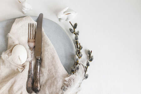 Stylish Easter table setting flat lay. Natural easter egg, pussy willow branches, feathers on modern...