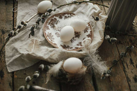 Rustic Easter still life. Natural egg in nest with feathers, vintage plate, cutlery, pussy willow...