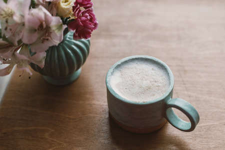 Spring morning aesthetics. Stylish ceramic cup of coffee and flowers on rustic wooden background. Ceramic vase with pink flowers and modern coffee cup.の写真素材