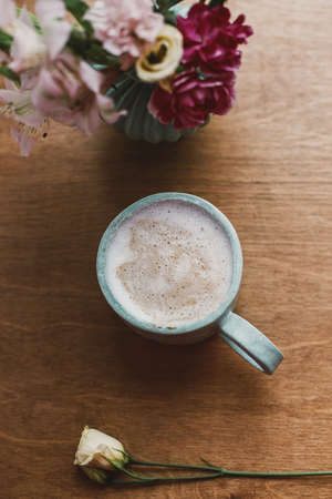 Stylish ceramic cup of coffee and flowers on rustic wooden background. Top view.  Ceramic vase with pink flowers and modern coffee cup. Spring morning aestheticsの写真素材