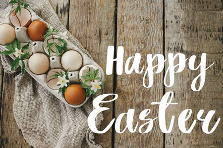 Happy Easter greeting card. Happy Easter text and natural eggs, blooming spring flowers, feathers, burlap on rural wood flat lay. Seasons greeting card, handwritten letteringの写真素材