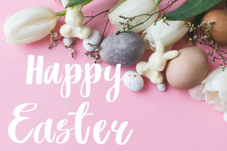 Happy Easter greeting card. Happy Easter text and modern stylish eggs, tulips, bunnies on pink background. Seasons greeting card, handwritten letteringの写真素材