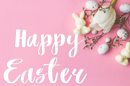 Happy Easter greeting card. Happy Easter text and modern eggs, tulips, bunnies flat lay on pink...