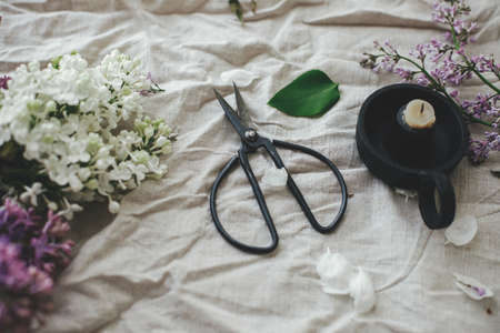 Beautiful lilac flowers, scissor, candle and petals on linen fabric composition. Spring floral still life on rustic background. Happy mothers dayの写真素材