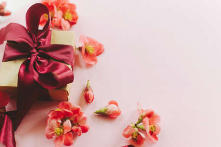 Stylish gift box with red flowers on pink background border. Happy Mothers day. Greeting card template with space for text. Festive craft gift with ribbon and flowers. Women's dayの写真素材