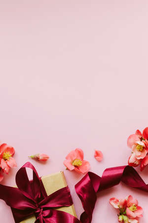 Stylish gift box with red flowers on pink background flat lay. Happy Mothers day and Women's day. Greeting card template with space for text. Festive craft gift with ribbon and flowers borderの写真素材