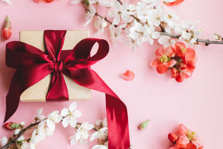 Stylish gift box with flowers on pink background flat lay. Happy Mothers day. Greeting card template. Composition of craft gift with ribbon, red flowers and cherry blossom. Women's dayの写真素材