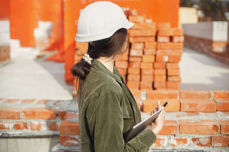 Stylish woman architect with tablet blueprints at construction site. Young female engineer or...