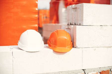 House building concept. Hard hats on autoclaved aerated concrete blocks at construction site. Safety...