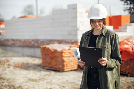 Stylish woman architect checking blueprints at construction site. Young female engineer or...
