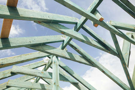 Unfinished roof trusses, view in attic with rafters and beams against sky. Wooden roof framing....