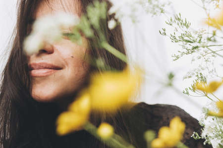 Beautiful sensual woman portrait in sunlight among summer wildflowers in room. Young brunette woman with flowers posing in sunlight. Skin care and self careの写真素材