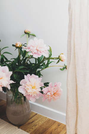 Beautiful peonies bouquet in modern boho room. Gentle pink peony flowers in vase on rustic background, moody image. Modern bohemian decor, stylish comfy interior detailsの写真素材