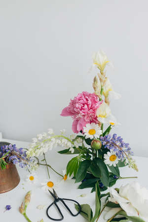 Modern summer flowers composition on rustic white table indoors. Creative floral image. Stylish...