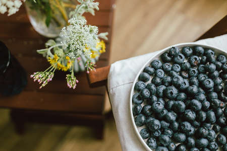 Fresh blueberries on modern ceramic plate and wildflowers bouquet in rustic room. Summertime in countryside. Healthy food aesthetics. Summer berries top viewの写真素材