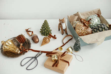 Stylish christmas vintage ornaments, gift, ribbon, scissors on rustic white table. Merry Christmas! Wrapping present aesthetic. Preparation for winter holidays, atmospheric time. Moody bannerの写真素材