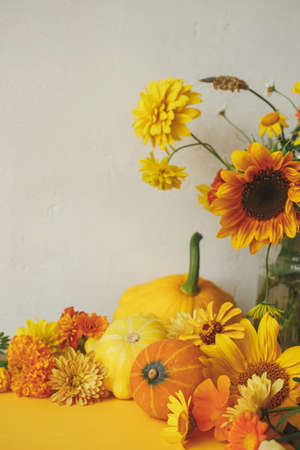 Stylish autumn composition on yellow paper against rustic background. Colorful autumn flowers, pumpkins, pattypan squashes on yellow. Seasons greeting card template with space for textの写真素材