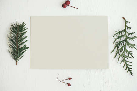 Christmas card flat lay. Empty greeting card mock up and fir branches, berries and christmas decorations on rustic white table. Postcard template with space for text. Happy Holidays!の写真素材