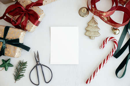 Christmas card mockup. Empty greeting card flat lay with christmas gift, decorations, ribbons, ornaments on white rustic table. Postcard template with space for text. Happy Holidays!の写真素材