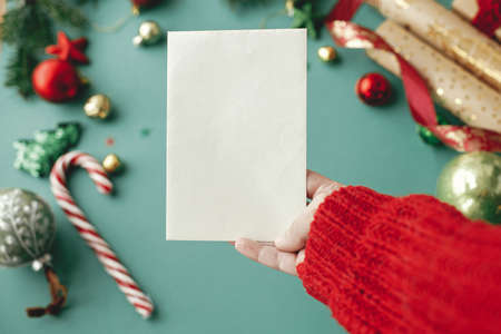 Hand holding christmas card mock up. Empty greeting card in woman hand on background of stylish...