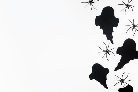 Halloween flat lay. Black ghosts and spiders decorations on white background. Happy Halloween! Card template with space for text. Stylish minimal borderの写真素材