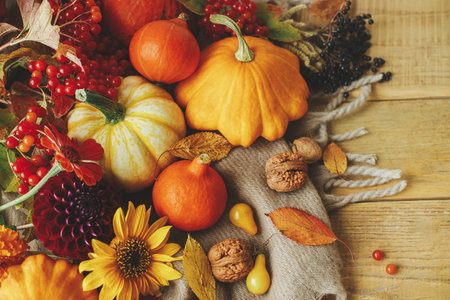 Happy Thanksgiving! Stylish pumpkins, autumn flowers, berries, leaves and nuts on cozy warm scarf on...