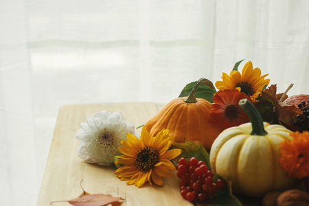 Autumn still life. Pumpkins, flowers, berries and nuts on rustic wooden table against window....