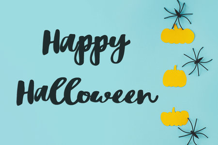 Happy Halloween! Happy Halloween text on black spiders and pumpkins on blue background flat lay. Creative greeting card, handwritten sign. Trick or treat!の写真素材