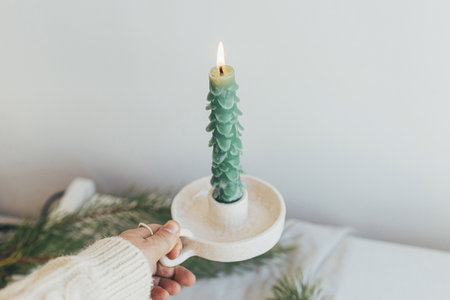 Hand holding stylish christmas candle as fir tree on background of white rustic table. Handmade modern green candle. Holiday advent. Merry Christmas!の写真素材