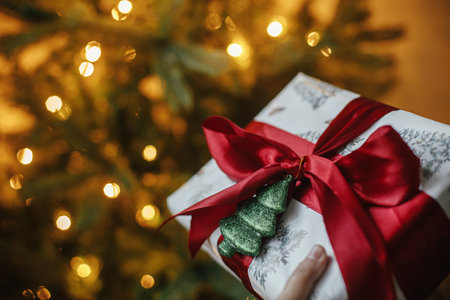 Merry Christmas and Happy Holidays! Stylish christmas gift at christmas tree with golden lights....