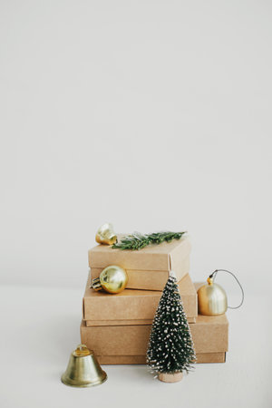 Merry Christmas! Stylish eco christmas gift boxes on white table. Simple craft christmas presents with golden baubles, tree and fir branch on rustic wood. Eco friendly holiday bannerの写真素材
