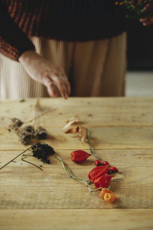 Making stylish autumn wreath on rustic table. Physalis, berries, herbs on wooden table. Details of fall decor and arrangement in farmhouseの写真素材