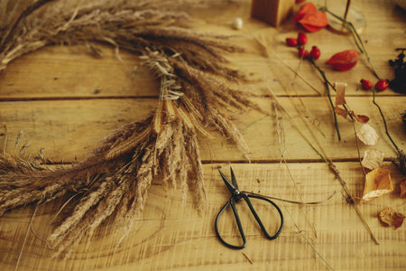 Stylish autumn wreath with dried grass, scissors, berries on wooden table. Making stylish autumn wreath on rustic table. Fall decor and arrangement in farmhouse.の写真素材